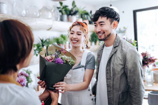 romantischer junger asiate kauft blumen für seine freundin im blumenladen, lächelt und plaudert mit dem floristen - people care surprise love stock-fotos und bilder