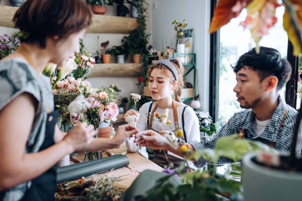 молодая азиатская пара посещает мастер-класс по цветочному глушению, создавая букет цветов с помощью опытного флориста. малый бизнес, худо� - florist flower arranging male стоковые фото и изображения