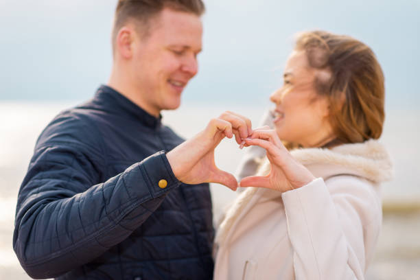 istock Two young couple is making heart, looking at each other and smiling while standing at the beach. 1366719865