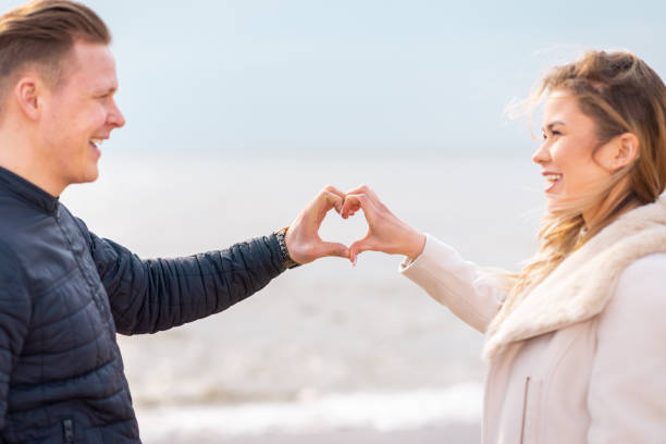 istock Two young couple is making heart, looking at each other and smiling while standing at the beach. 1366719868