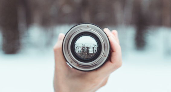 Looking to the frozen lake in middle of forest through lens. Point of view. Selective focus.