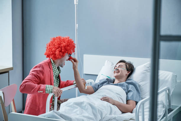 Clown with patient at hospital ward Sick young woman lying on bed and laughing while the clown entertaining her during the treatment at hospital clown photos stock pictures, royalty-free photos & images