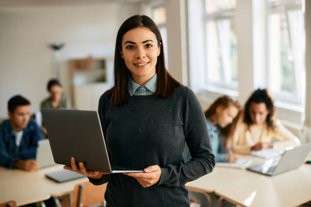 insegnante di informatica sorridente che usa il laptop durante una lezione e guarda la fotocamera. - teaching foto e immagini stock