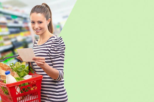 Woman at supermarket holding a full shopping basket and a shopping list, blank copy space