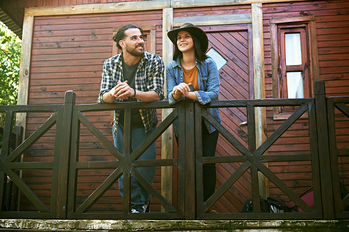 Low angle full length view of man and woman in weekend attire leaning on railing, looking at view, and smiling.