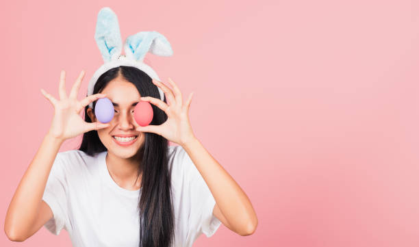 istock woman smiling wearing rabbit ears holding colorful Easter eggs front eyes 1366734090
