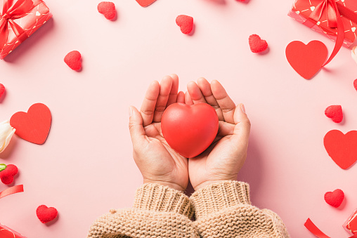 Valentine's day and birthday. Woman hands holding red heart and have gift or present box decorated surprise on pink background, Female's hand hold heart have gift box package in craft paper