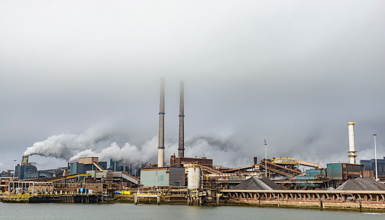 Steel mill in IJmuiden The Netherlands part of the Tata Steel Europe steel factory located on the Dutch coast during a cloudy day. Thick smoke is coming from the cimneys.