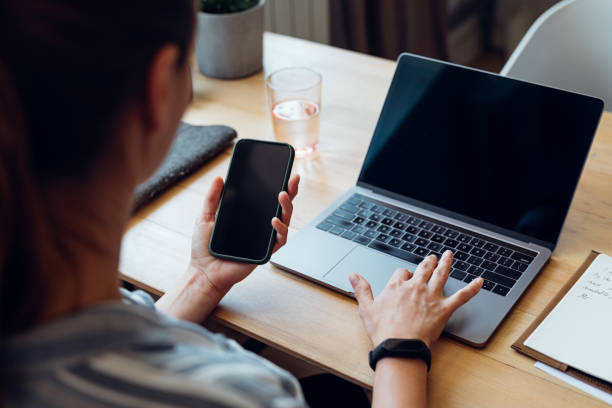 Unrecognizable Women Looking at her Mobile Phone while Typing Notes on the Laptop (Copy Space)
