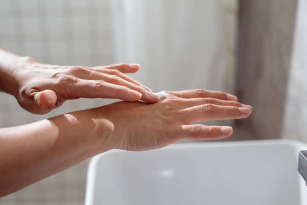 anonimo giovane donna caucasica che applica una crema per le mani in bagno - contemporary domestic room sparse indoors foto e immagini stock