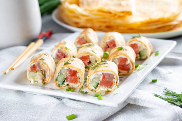 Thin pancake rolls or crepes rolls with smoked salmon, cream cheese, cucumber and dill on a gray concrete background. Maslenitsa.