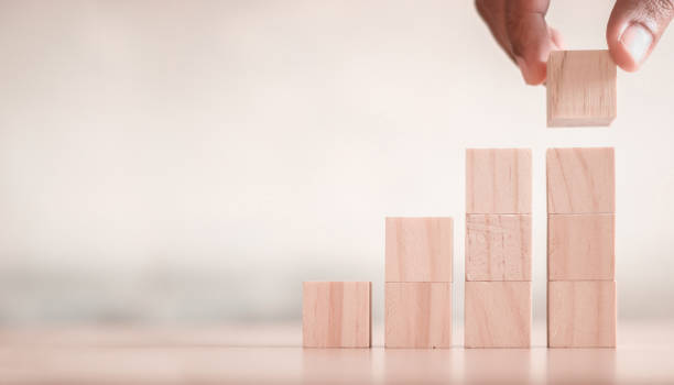 istock Hand arranging wood block stacking as step stair on wooden table. 1366742435