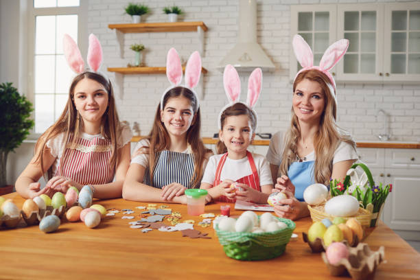istock Happy easter. Mother and daughters with rabbit ears decorate Easter eggs at a table in kitchen. 1366744803