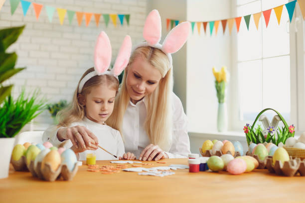 istock Happy easter. Daughter and mother with rabbit ears decorate Easter eggs sitting at a table 1366745401