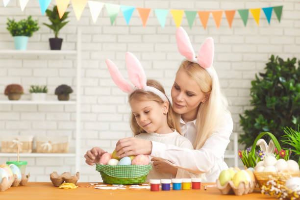 istock Happy easter. Daughter and mother with rabbit ears decorate Easter eggs sitting at a table 1366745407