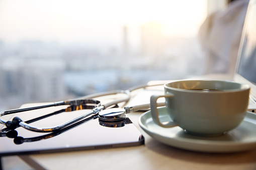 A coffee cup with a stethoscope and laptop at wooden table
