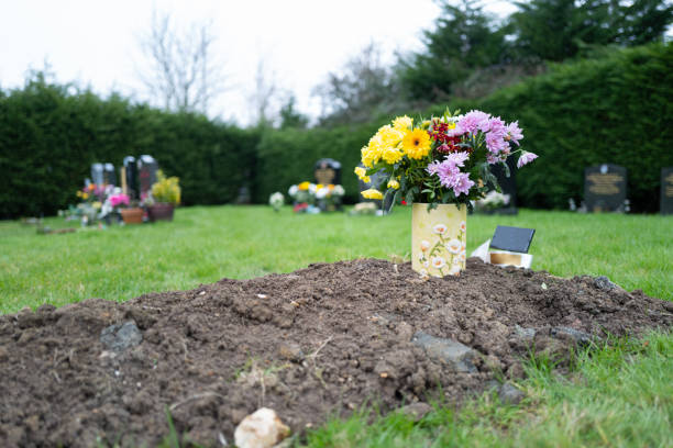 Freshly dug grave in q quiet cemetery. The grave is unmarked and shows a fresh bunch of yellow flowers on the soil heap.