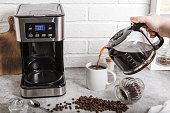 A woman's hand pours coffee from a coffee pot into a cup. Home life. Electric coffee maker on the kitchen countertop