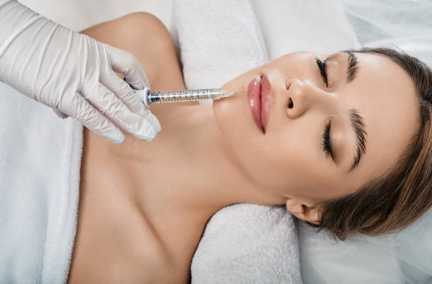 Woman while procedure lip augmentation at cosmetology clinic with beautician. Filler injection for beautiful female lips augmentation with hyaluronic, top view stock photo