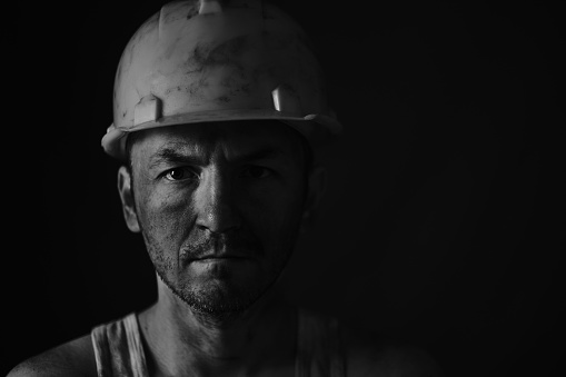 Portrait miner in helmet and undershirt with dirty face