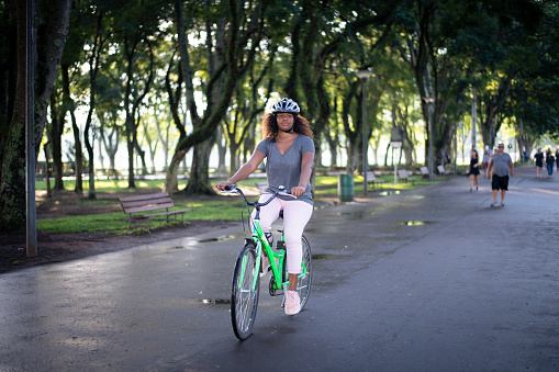 Young black woman commuting by bike in a park back home after working