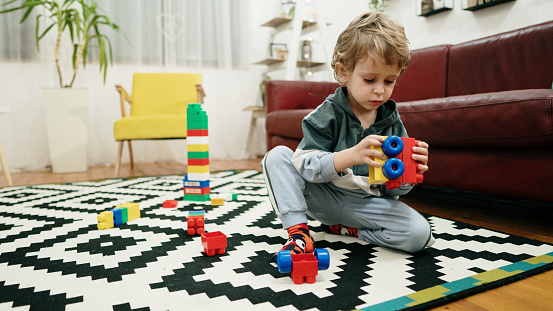 Beautiful toddler boy playing with construction blocks at home