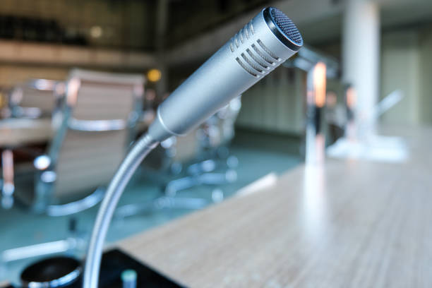 istock Wide angle side close-up of a microphone on a table in a conference room, lecture hall or boardroom with selective focus and lot of copy space 1366760993