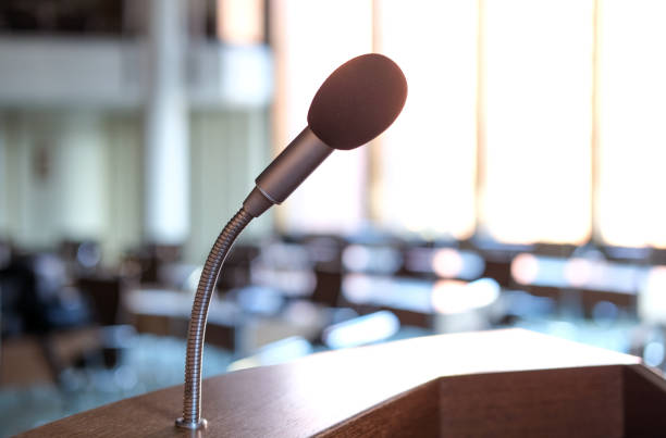 istock Concept communication and media: Empty conference hall or meeting room with focus on the speaker's desk microphone in the backlight 1366761003