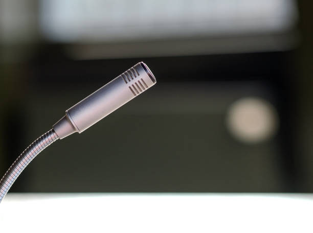 Detail of an isolated silver microphone in a board or conference room or office, side view and blurred background Isolated close-up side view of a microphone in a meeting room, conference hall or office with chairs and table in the blurred background, selective focus, copy space interview seminar microphone inside of stock pictures, royalty-free photos & images