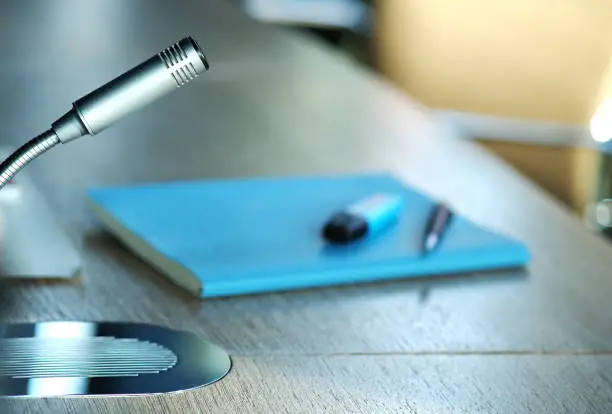 Photo of Isolated silver microphone on a table in a board or conference room or office with documents, files, papers and writing materials in the background