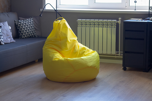 Yellow upholstered bag chair in the interior of a gray dark modern room of a teenage boy or a living room.
