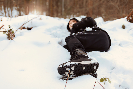 Photo of a men with hypothermia lying down surrounded by frozen winter landscape. Young man blowing in his hands to warm up in the cold winter environment. Cold and loneliness.