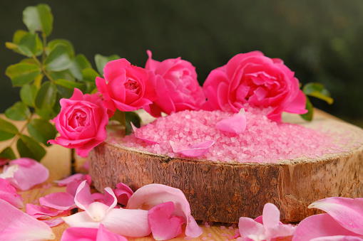 Rose cosmetics salt on a wooden saw cut on a green garden background.Aromatherapy and cosmetics.rose flowers and pink cosmetics salt.Organic salt with rose extract