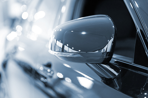 A close-up, centered picture of the right-hand side mirror of a new dark blue car. Light is visible on the highly reflective body of the car.