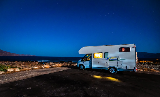 Motorhome RV parked under stars on a pier by the sea, Crete, Greece. Travelers with camper van are resting overnight on an active family vacation in Kissamos, Crete, Greece.