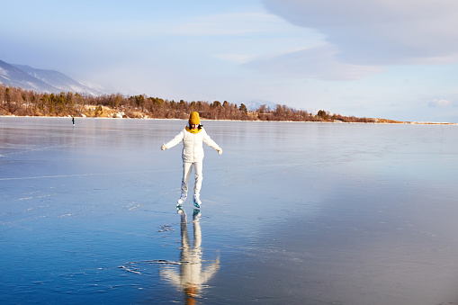A young athletic girl is skating on the transparent ice of the frozen Lake Baikal. The concept of active winter recreation and sports.
