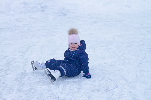 Baby girl caucasian learns to skate at the ice rink in winter falls and laughs.