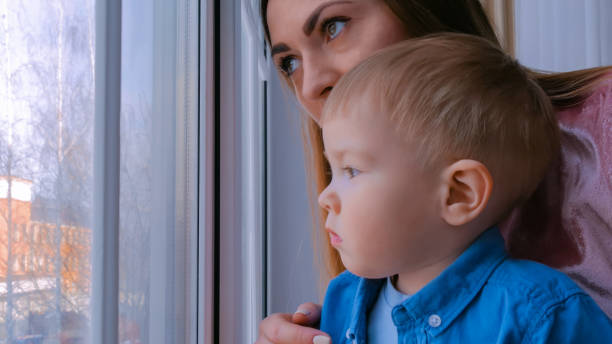 istock Young mother and pensive little boy looking through window 1366769763