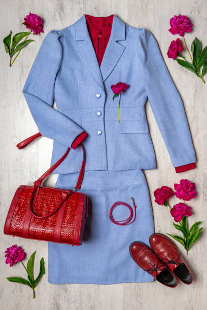 Women classic suit in blue color with red accessories and peonies on light background. Jacket and skirt with blouse, handbag and shoes. Spring flowers. Beautiful stylish clothes, fashionable outfit