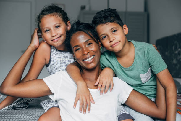 Family hug Beautiful african-american mother hugging her two adorable children in bedroom. mom and sister stock pictures, royalty-free photos & images