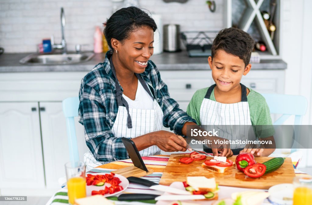 Mother and son in the kitchen Young african-american mother and her cute son preparing healthy and tasty sandwiches together in the kitchen. Cooking Stock Photo