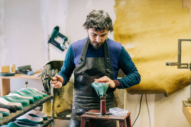 Young shoemaker in the workshop. Shot of confident craftsperson making a leather luxury shoes in his workshop. cobbler stock pictures, royalty-free photos & images