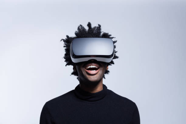 Happy young man using virtual reality glasses Portrait of excited afro american man wearing virtual reality glasses, standing against grey background and laughing. virtual reality simulator stock pictures, royalty-free photos & images