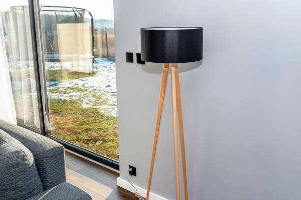 a modern and simple lamp standing on three wooden legs against a gray wall and a large terrace window. - switch yard imagens e fotografias de stock