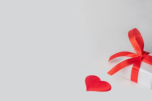 white background for valentine's day fragment of a gift box with a red ribbon and a heart.