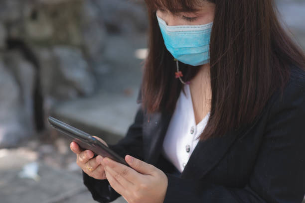 istock business woman wearing face mask using smartphone tablet in calling for working with her customer in park with sunrise and blur nature background. business new normal with corona virus or covid-19. 1366783326