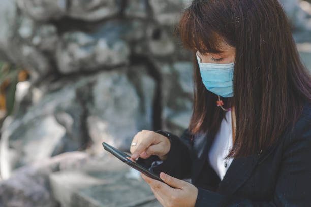 istock business woman wearing face mask using smartphone tablet in calling for working with her customer in park with sunrise and blur nature background. business new normal with corona virus or covid-19. 1366783327