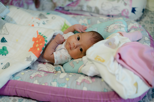 Newborn baby girl lying in colorful baby nest and looking at the camera