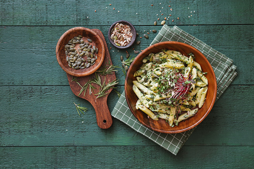 Vegetarian penne with zucchini, arugula, seeds, vegan cheese and pesto sauce. Flat lay top-down composition on dark green background.