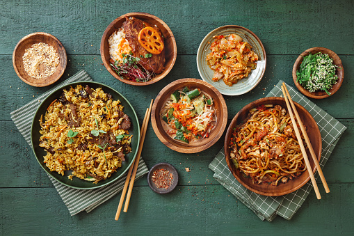 Spicy Korean beef noodles (Shin Ramyun). Korean BBQ pork ribs with rice. Fried rice with beef. Flat lay top-down composition on dark green background.